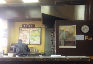 The pizza master, Dom De Marco, at work next to a painting of him at work. Craig Nelson, 2014.